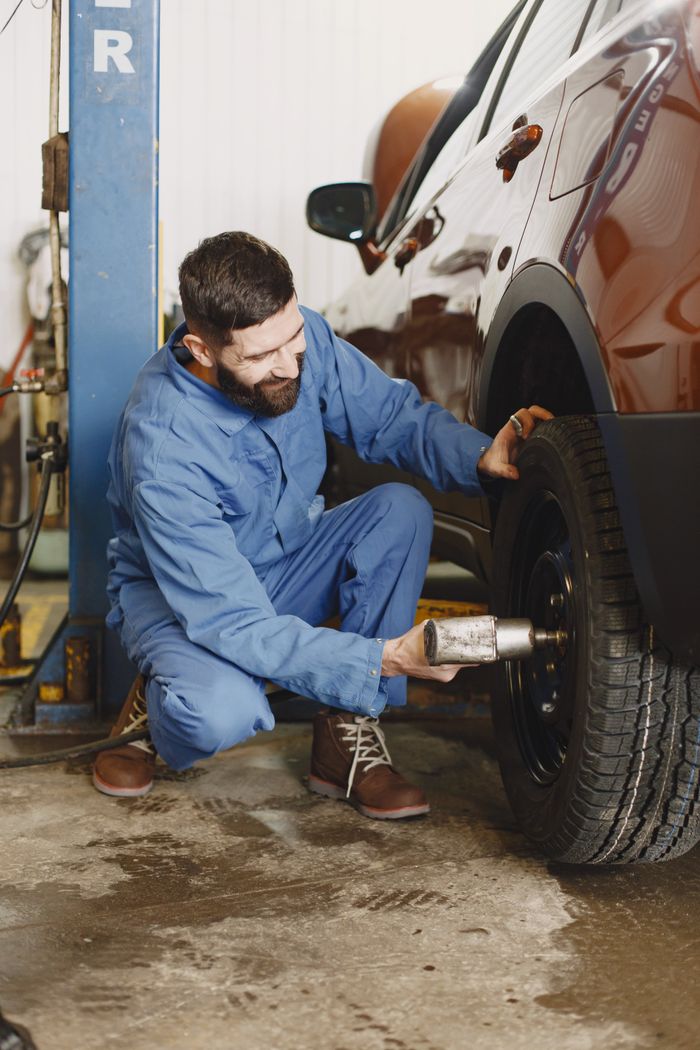 Mechanic kneeling to repair a car tire in a professional garage setting.